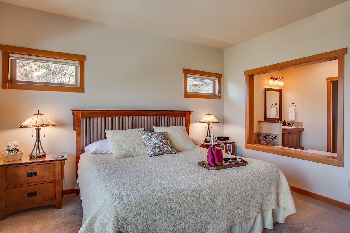 A neatly arranged bedroom with a large bed, two bedside tables, a nightstand, a window, and a mirror.