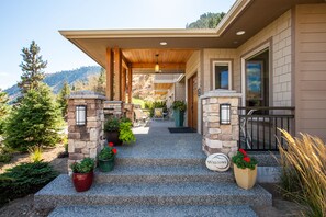Una casa moderna con fachada de piedra, un letrero luminoso que dice 'Welcome' y un porche cubierto con mobiliario exterior.
