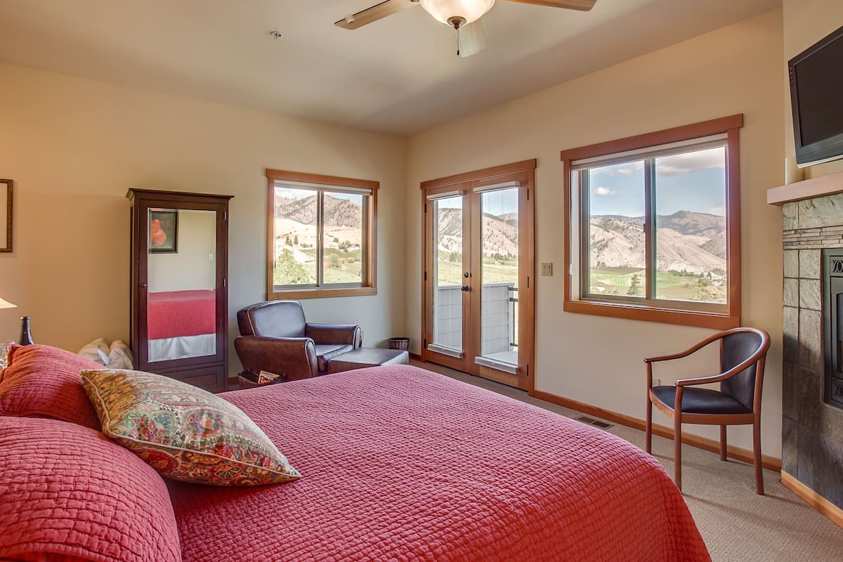 A bedroom with a large bed, a chair, a desk, and a fireplace.