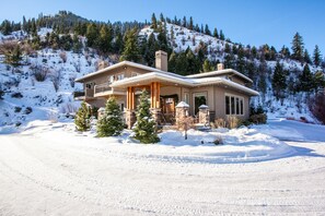 Una casa de dos pisos con un porche cubierto, rodeada de un paisaje nevado y árboles.