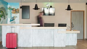 Een modern receptiebalie met een flatscreen televisie, een stadslandschap schilderij en een rode koffer.
