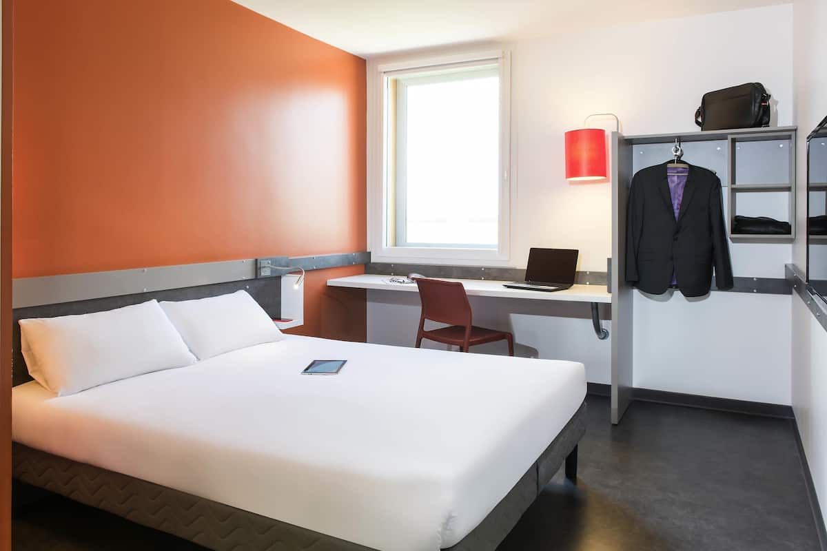 Ein Hotelzimmer mit Bett, Schreibtisch, Stuhl, Laptop, roter Lampe und Kleiderhaken.