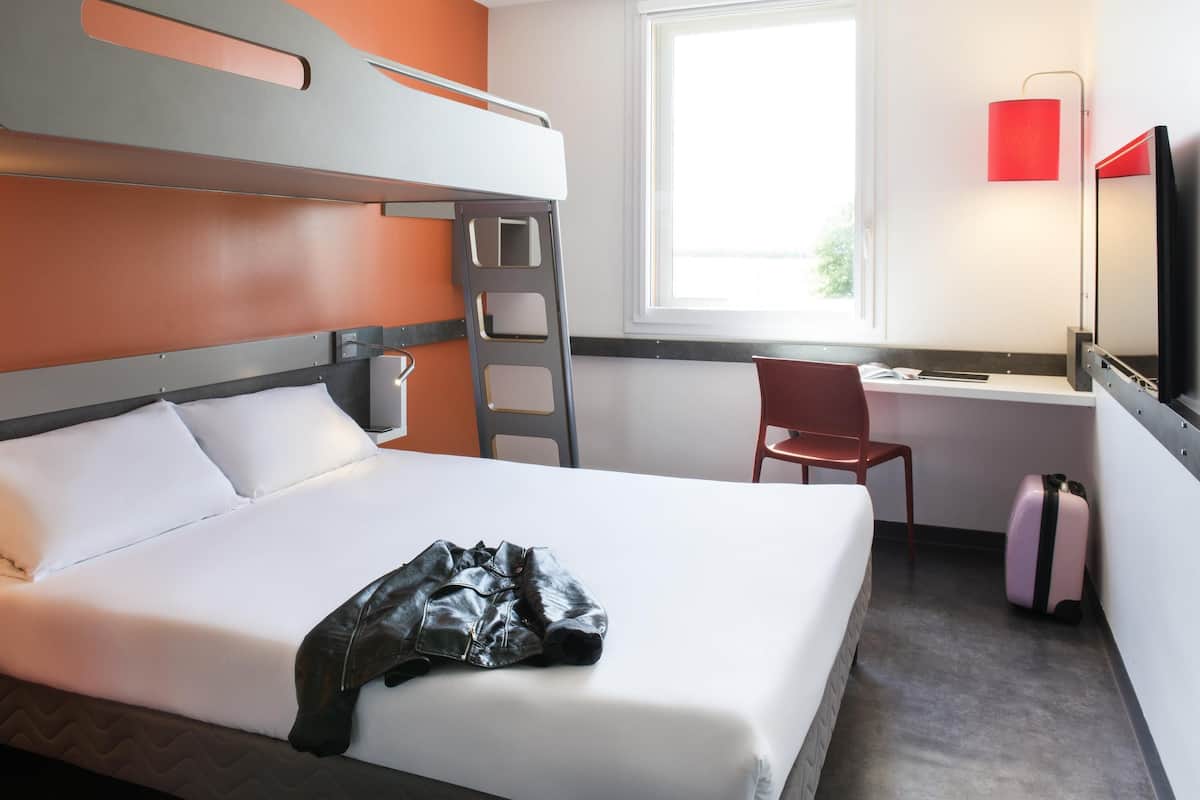 Ein Stockbett mit einer Leiter, ein Schreibtisch mit Stuhl, ein Fernseher und ein Koffer.