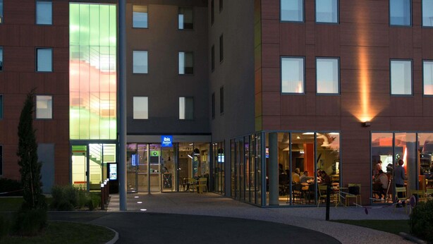 Een modern gebouw met een glazen ingang, een bord met de tekst 'ibis budget' en meerdere ramen.