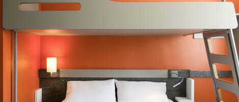 A bunk bed with a ladder, a bedside table with a lamp, and a headboard against an orange wall.