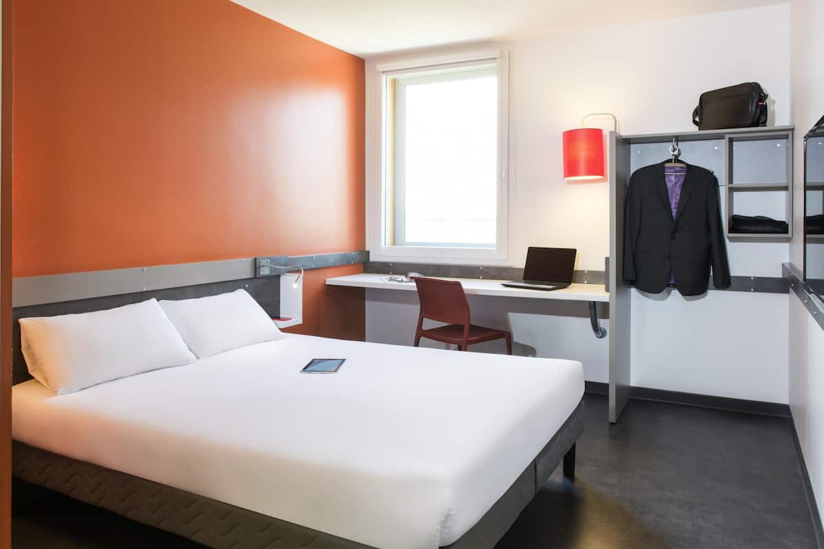 Une chambre d’hôtel équipée d’un lit, d’un bureau, d’une chaise, d’un ordinateur portable et d’un porte-manteau.
