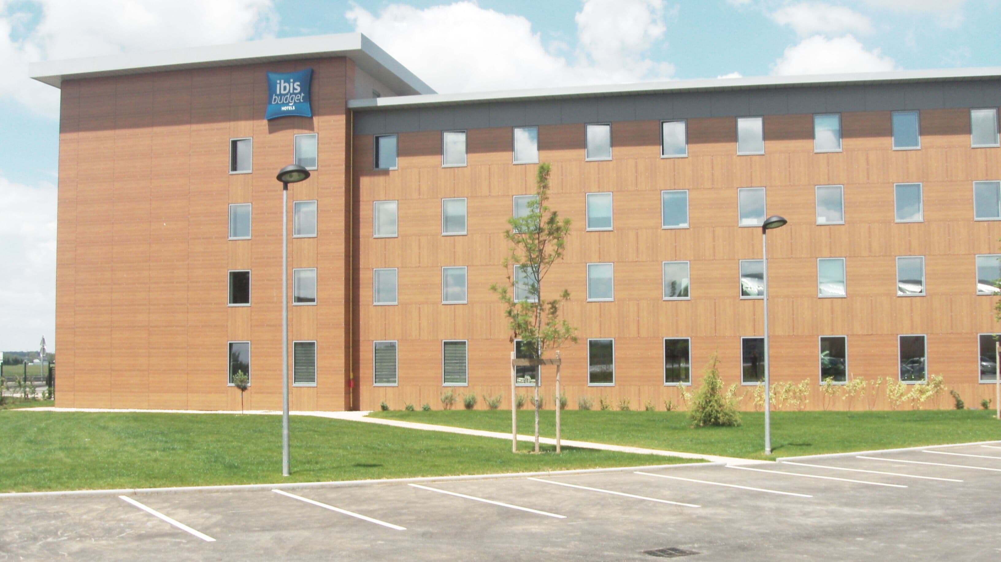 A modern hotel building with a flat roof, multiple windows, and a sign for 'ibis budget hotels'.