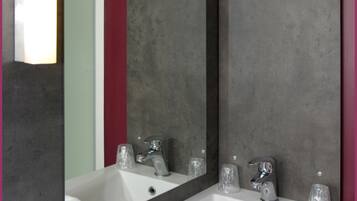 Un baño moderno con un espejo grande, lavamanos blanco y dos grifos.