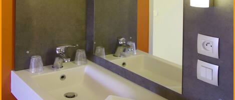 A bathroom with a white sink, two faucets, a mirror, and a towel rack.