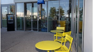 Een hotelentree met glazen deuren, een blauw bord en gele stoelen.