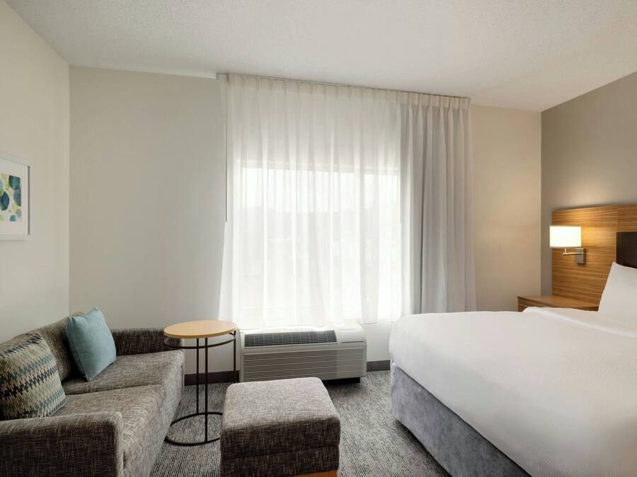 A hotel room with a bed, a sofa, a small round table, and a wall-mounted lamp.