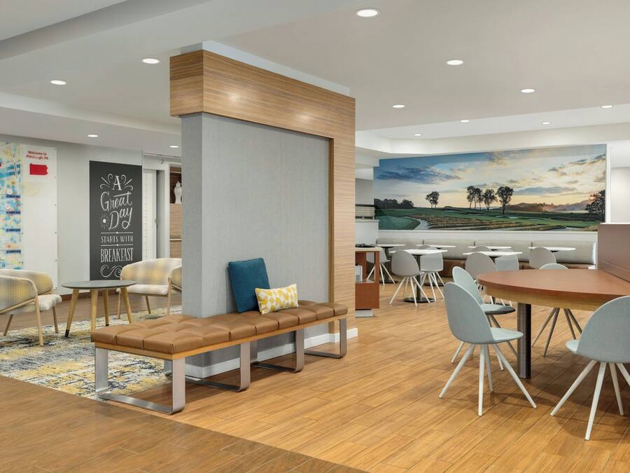 Un comedor moderno con un banco de madera, sillas grises y un cuadro grande de un paisaje.