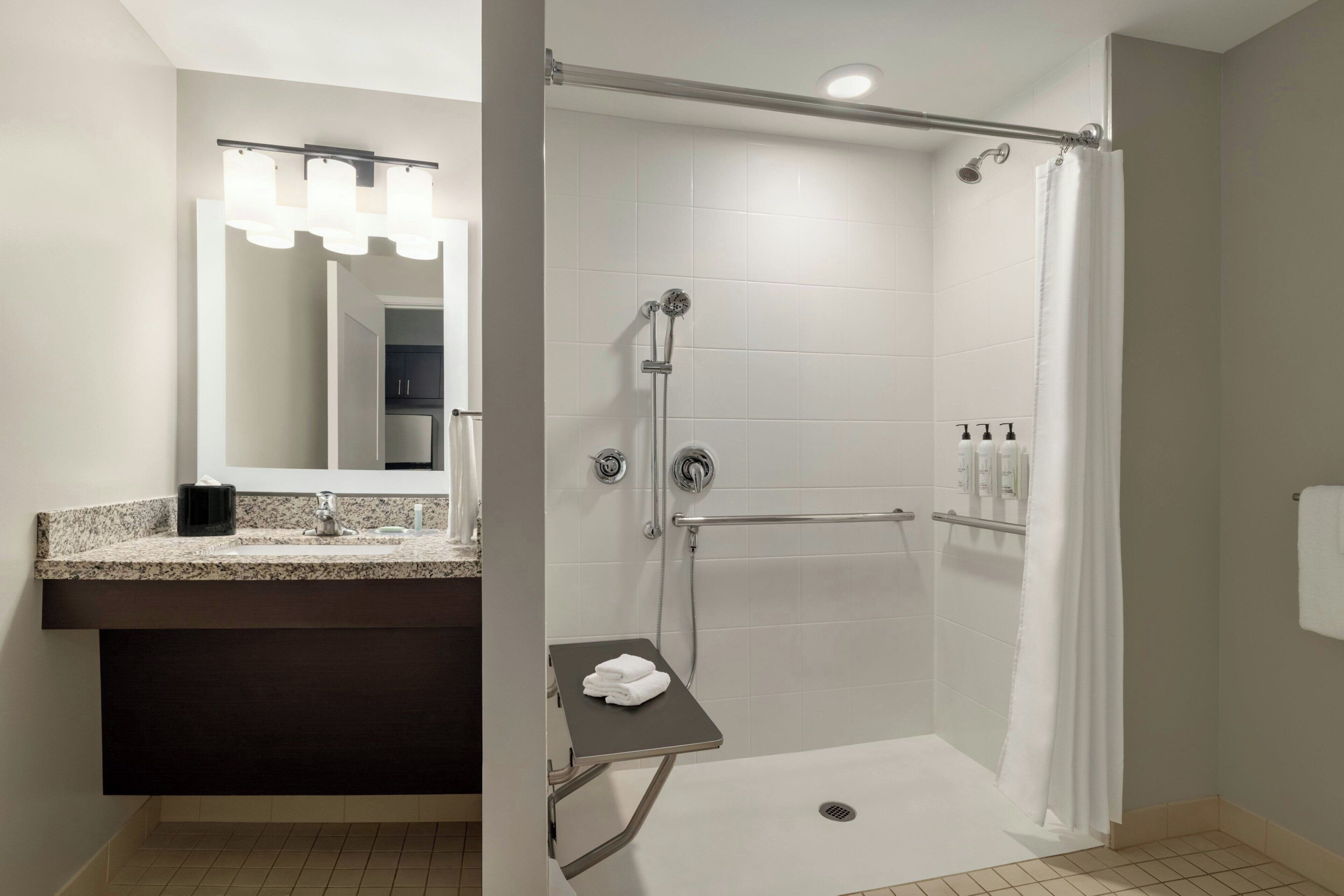 A modern bathroom with a vanity, a shower with a grab bar, and a towel rack.