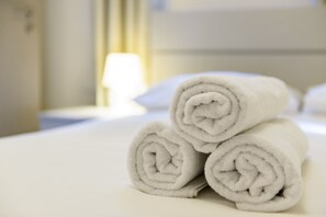 Una cama bien hecha con toallas blancas enrolladas apiladas encima.