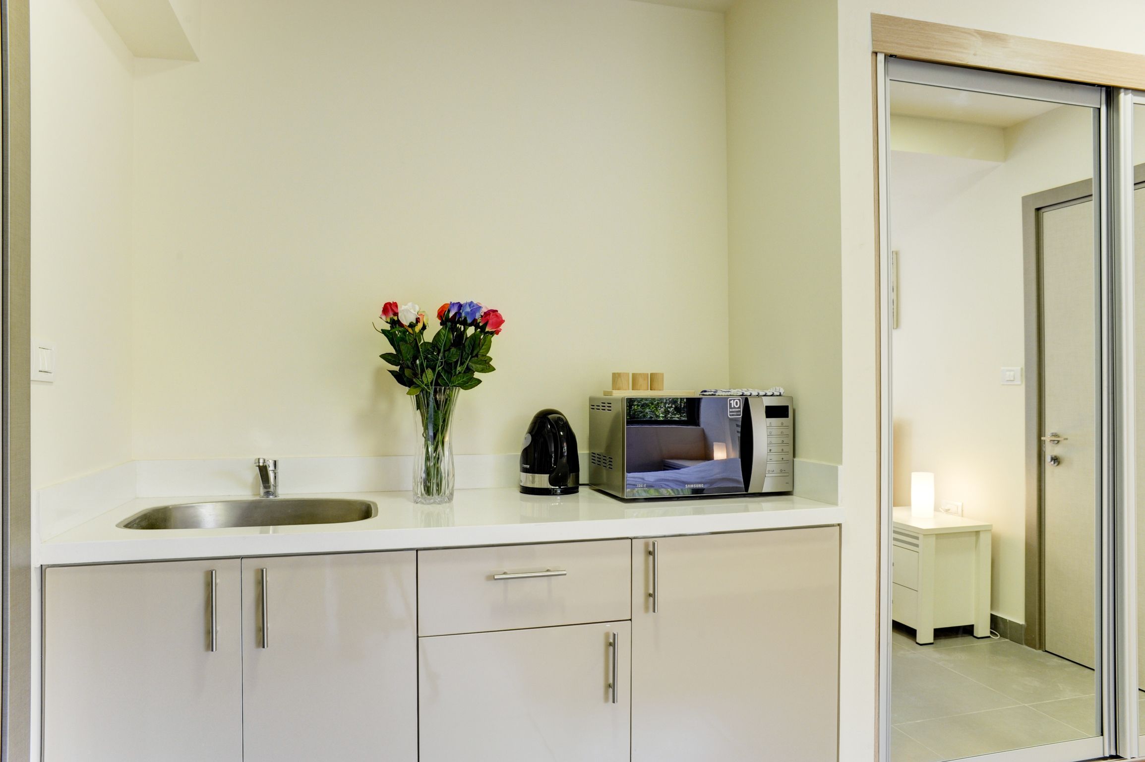 A modern kitchen with a stainless steel sink, a kettle, a microwave, and a vase with flowers on the counter.