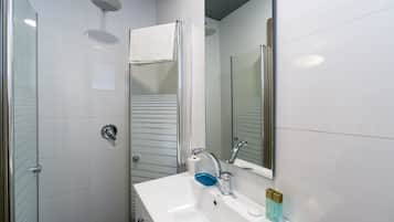 A modern bathroom with a glass shower enclosure, a white sink with a blue soap dish, and a large mirror.
