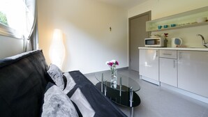 A modern living room with a glass coffee table, a black sofa, and a view of a kitchen area with white cabinets and a microwave. - Dizengoff Inn (Tel Aviv)