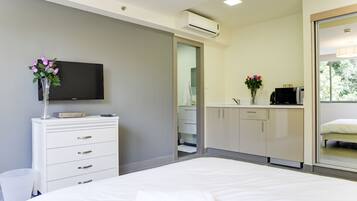 Una habitación de hotel moderna con una cama, un televisor en una cómoda y un baño visible a través de una puerta abierta, además de una ventana con vistas a zonas verdes.