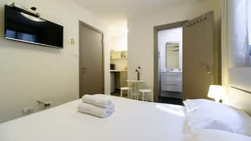 Et hotelværelse med seng, fjernsyn ophængt på væggen, et skrivebord med stol og et badeværelse, der kan ses gennem en åben dør.