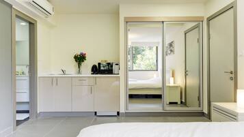 A modern bedroom with a large bed, a built-in wardrobe, a vanity with a mirror, and a small kitchenette area.