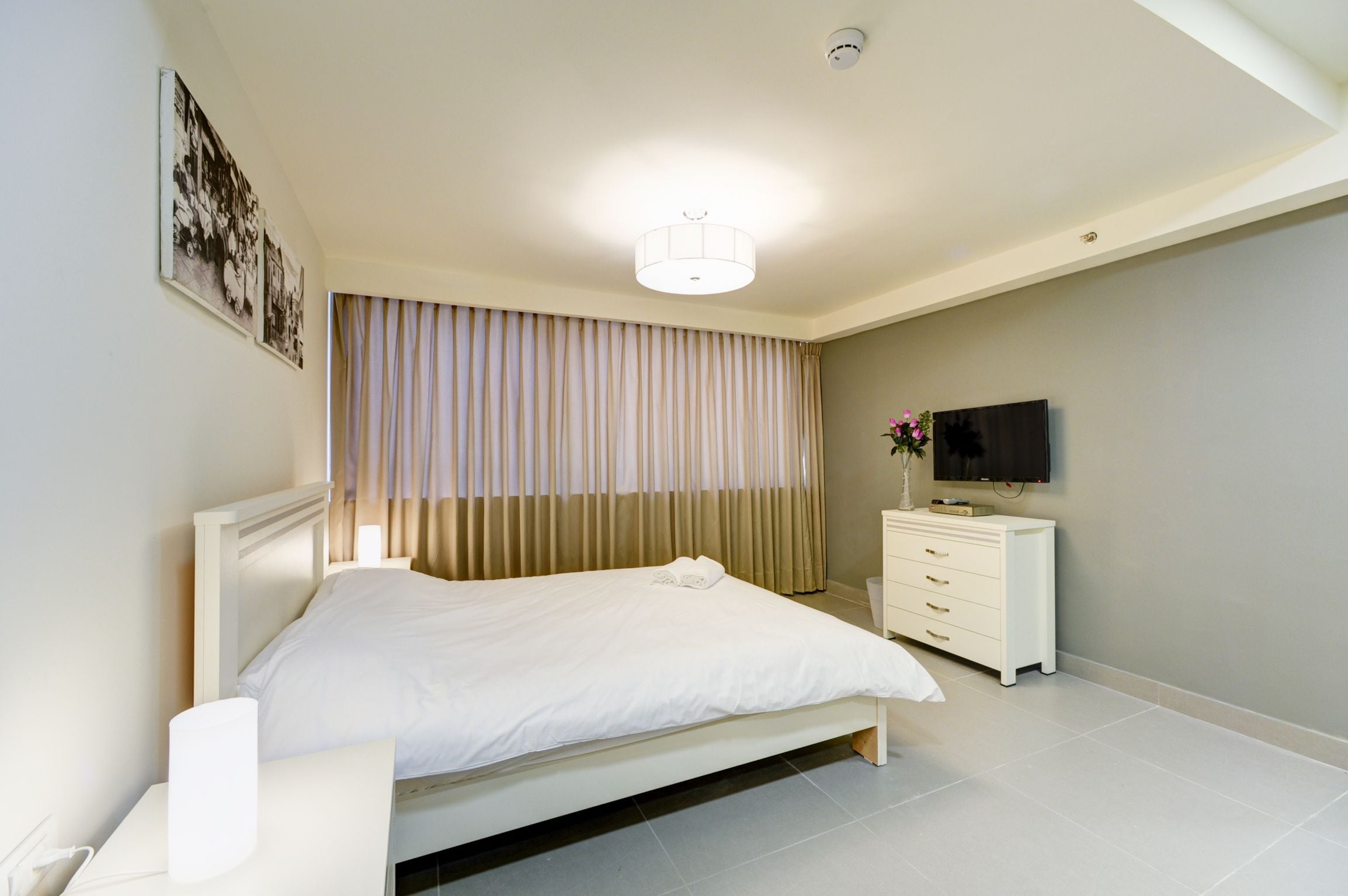 A modern hotel room with a large bed, a bedside table, a TV, and a dresser.