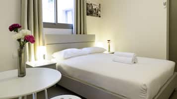A hotel room with a bed, a bedside table with a lamp, a small round table, and a vase with flowers.