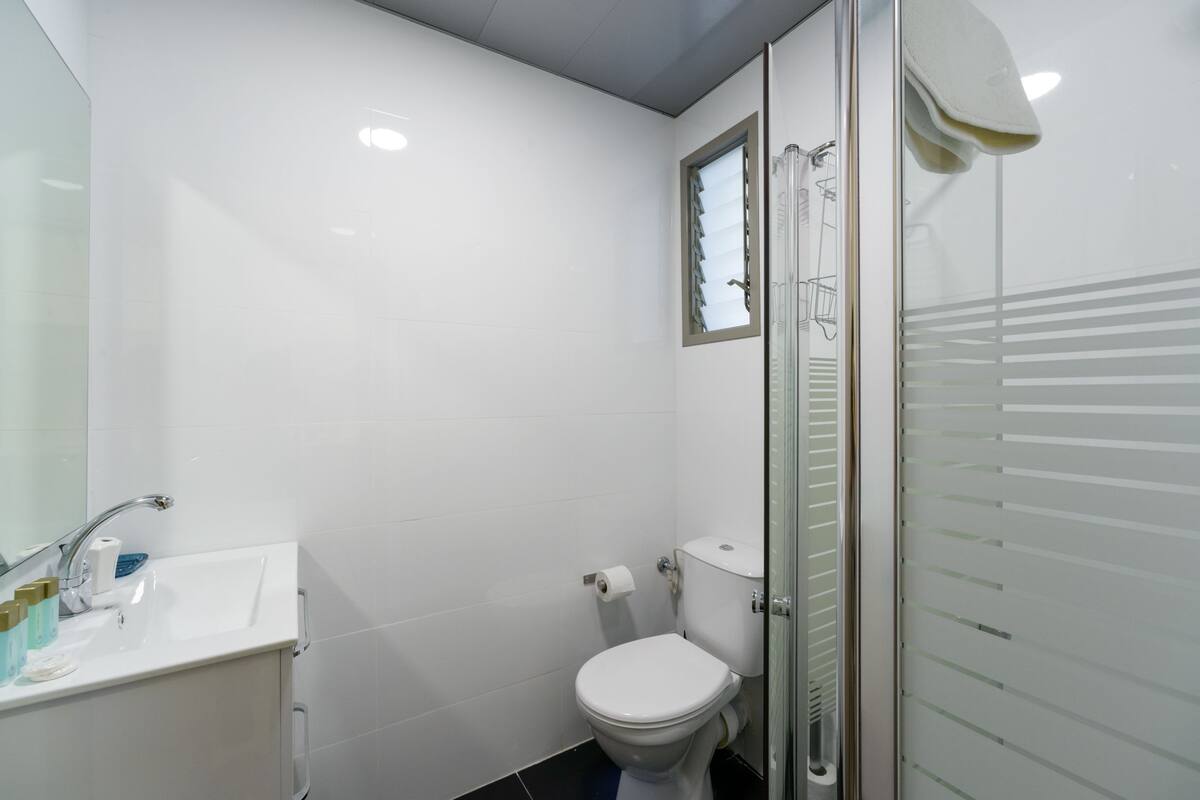 Ein kleines, modernes Badezimmer mit Waschbecken, Toilette und Dusche, alles in Weiß.