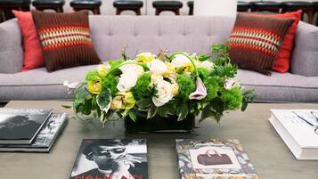 A sofa with patterned cushions, a floral arrangement on a table, and books with visible titles.