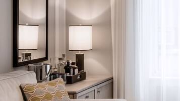 A hotel room with a sofa, a side table with a lamp, a mirror, and a window with curtains.
