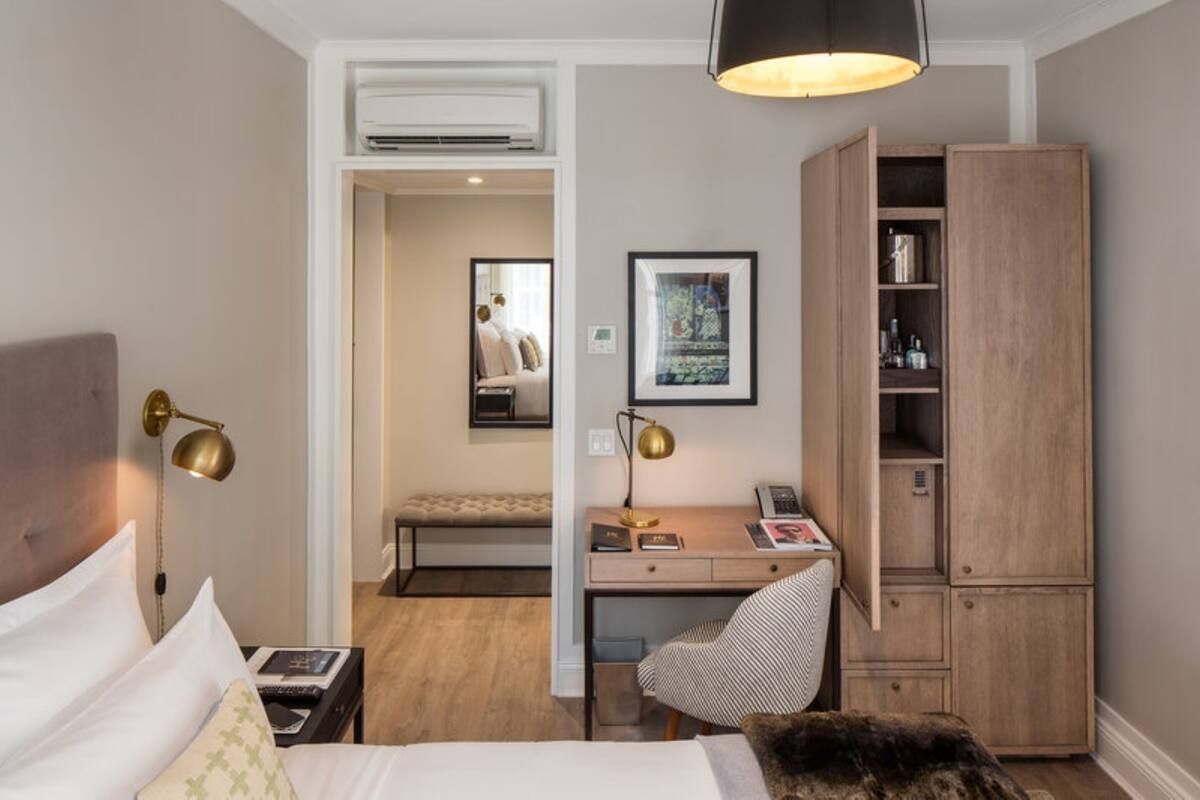 A hotel room with a bed, desk, chair, wardrobe, and a small sitting area with a bench.