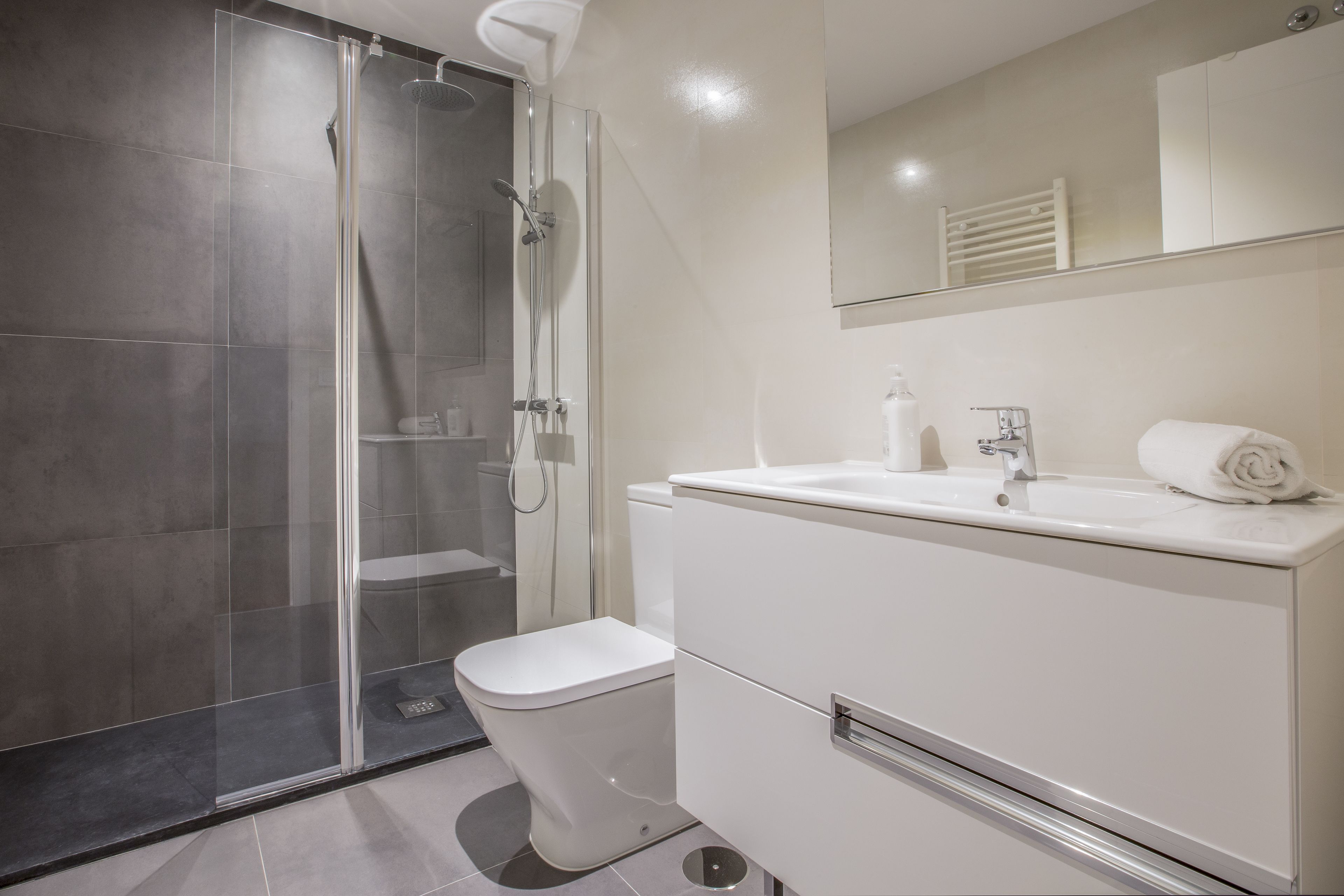 Un baño moderno con ducha envuelta en vidrio, inodoro blanco y lavamanos con espejo.