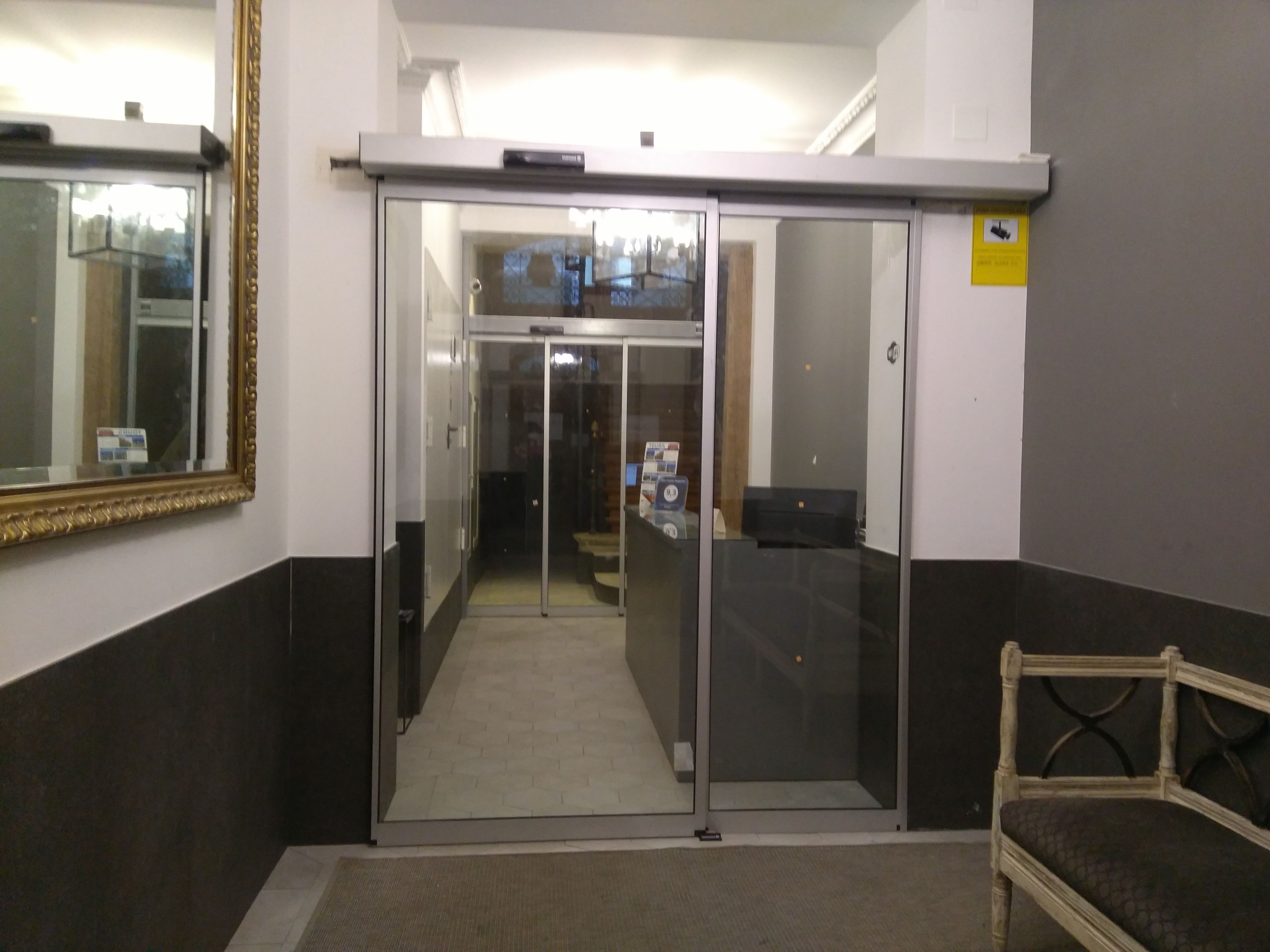 A hallway with a sliding glass door leading to a room, a chair, and a mirror on the wall.