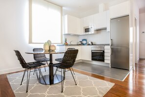 A modern kitchen with white cabinets, a stainless steel refrigerator, a microwave, and a dining area with a round table and black chairs.