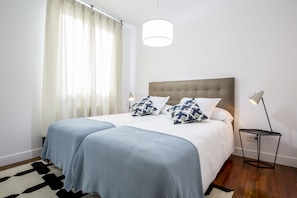 A neatly arranged bedroom with a large bed, a bedside lamp, and a window with curtains.