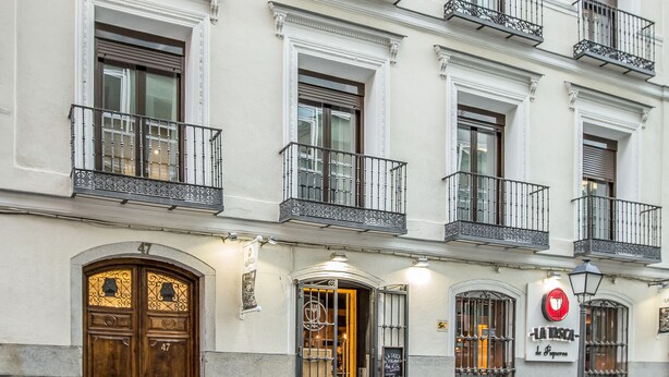 A multi-story building with ornate balconies, a prominent entrance with a wooden door, and a sign indicating a restaurant. - Slow Suites Augusto (Madrid)
