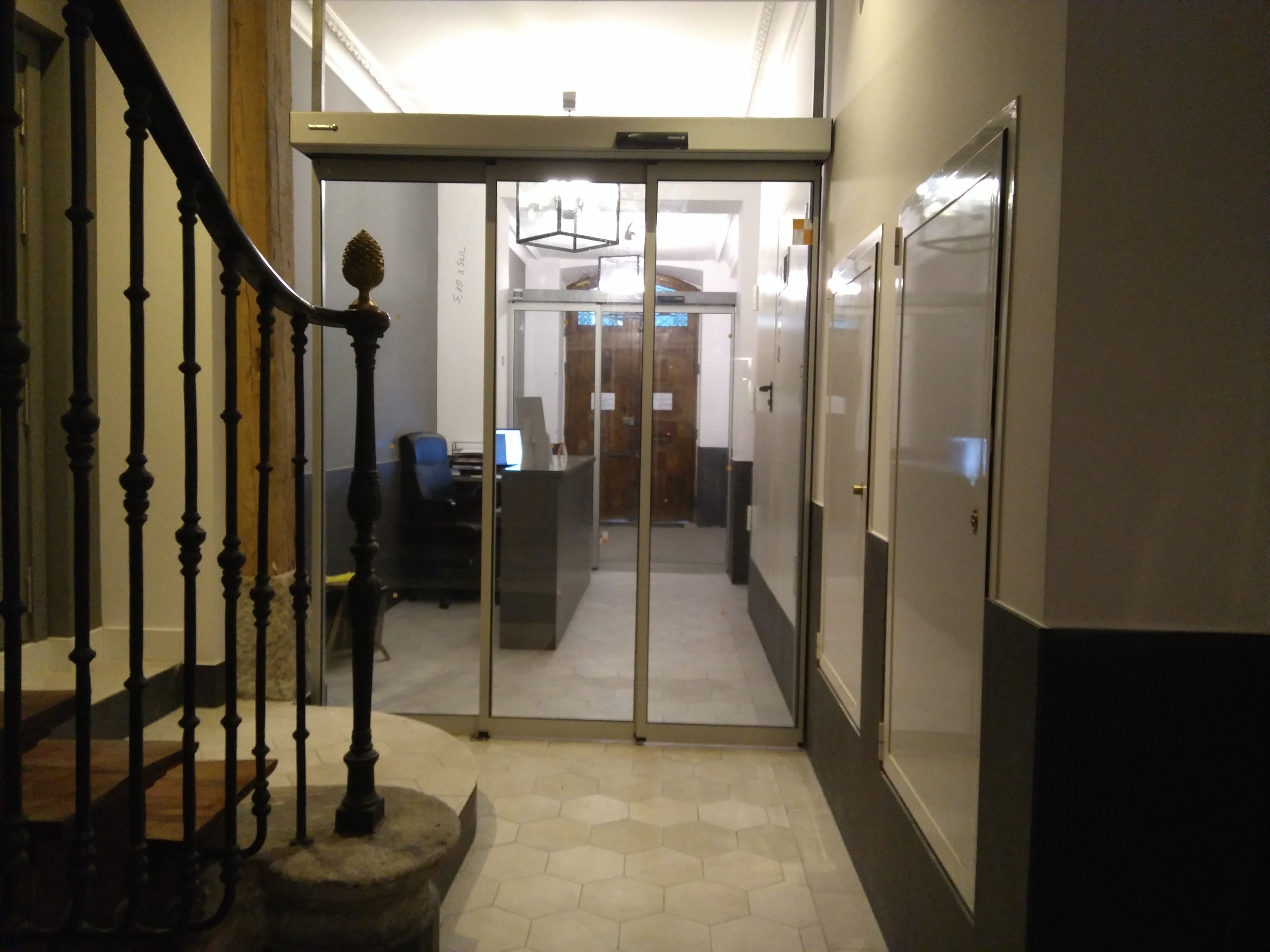 A modern interior with a staircase, a reception desk, and a glass door leading to another room.