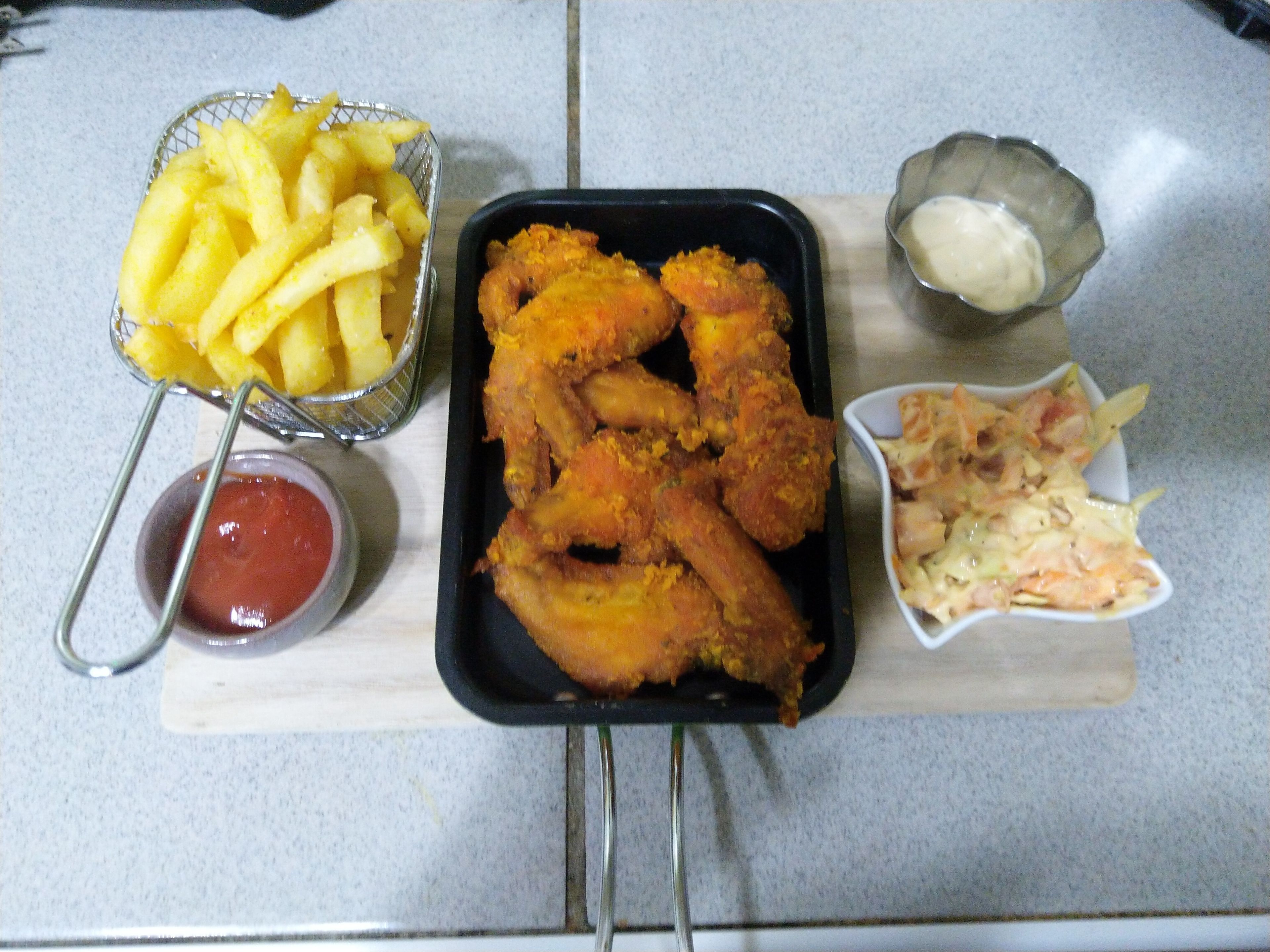 Una bandeja con alitas de pollo fritas, papas fritas, ensalada de col y un recipiente pequeño de kétchup.