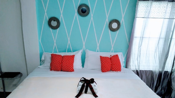 Una cama con ropa de cama blanca y roja, un lazo y una pared verde azulada con patrones geométricos.