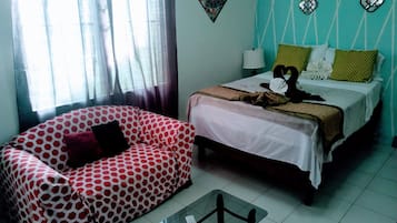 A room with a patterned sofa, a bed with pillows, a bedside table, and a window with curtains.