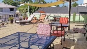 Un patio al aire libre con una mesa de vidrio, varias sillas con cojines estampados y una sombrilla amarilla.
