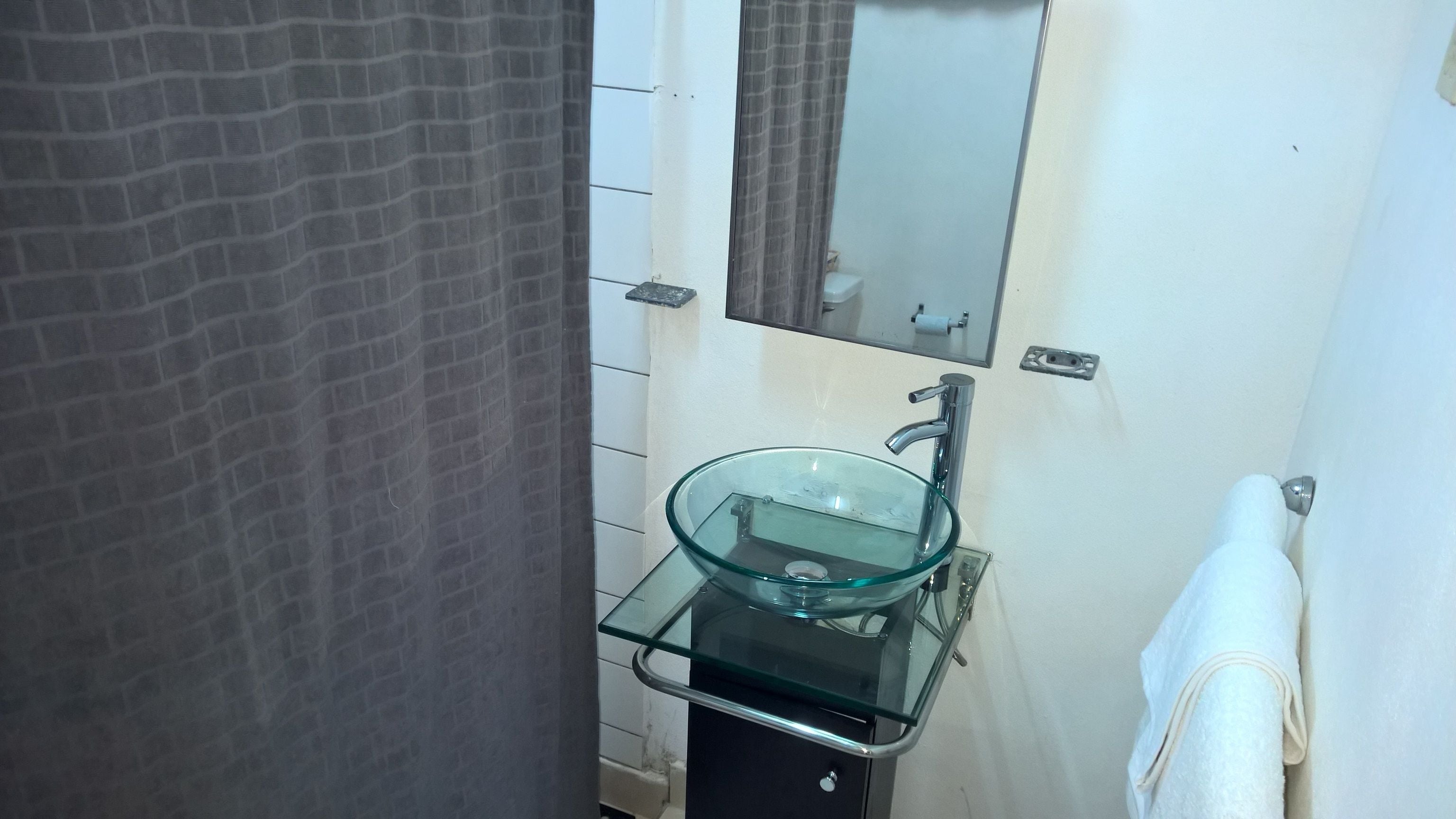 Un baño con un lavabo de vidrio, un espejo encima y una toalla colgada en la pared.
