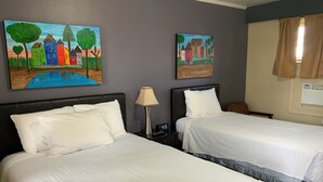Une chambre d’hôtel avec deux lits, une table de chevet avec une lampe et deux tableaux au mur.