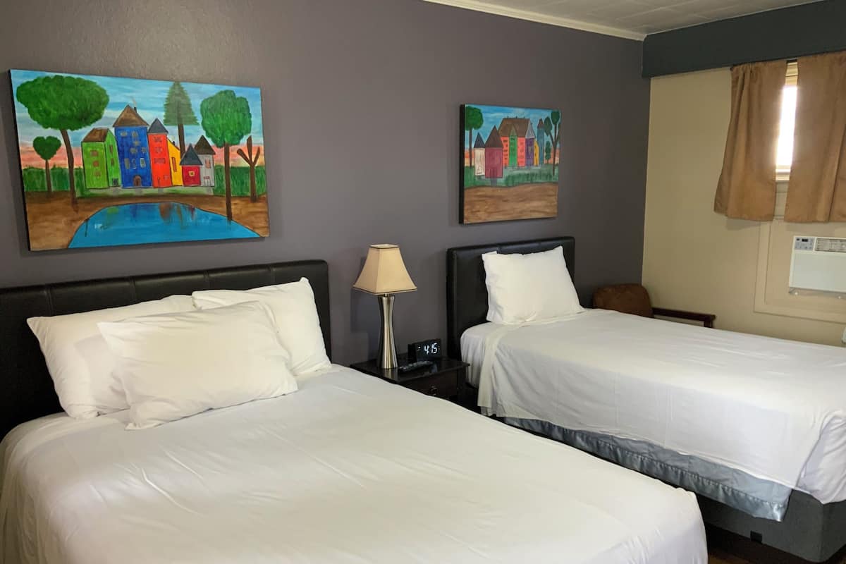 A hotel room with two beds, a nightstand with a lamp, and two paintings on the wall.