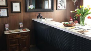 Un espace d’accueil avec un mur lambrissé en bois, un grand miroir, des trophées encadrés, un petit meuble avec des tiroirs, un vase avec des fleurs et un lustre.