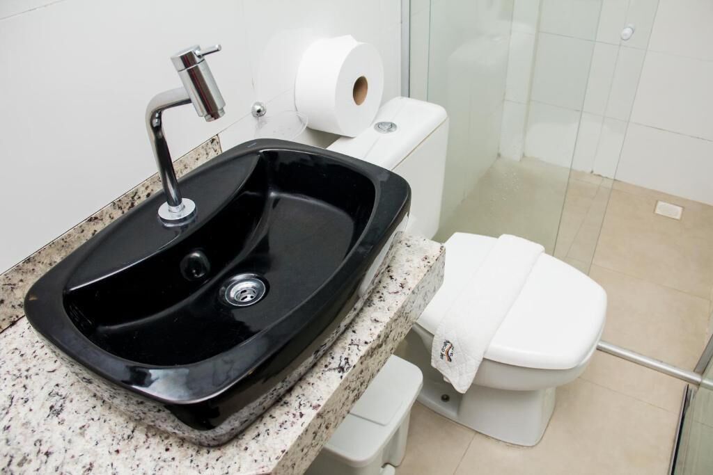 Un baño con un lavabo negro, inodoro blanco y un rollo de papel higiénico.