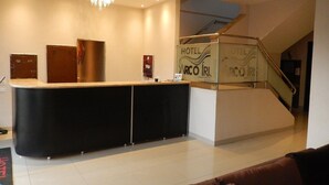 Un hall d’hôtel avec un comptoir d’accueil noir, un lustre, un escalier et une enseigne indiquant « Hôtel Arco Iris ».