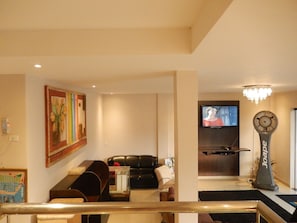 Una sala de estar con un sofá de cuero negro, una mesa de comedor y un televisor montado en la pared.
