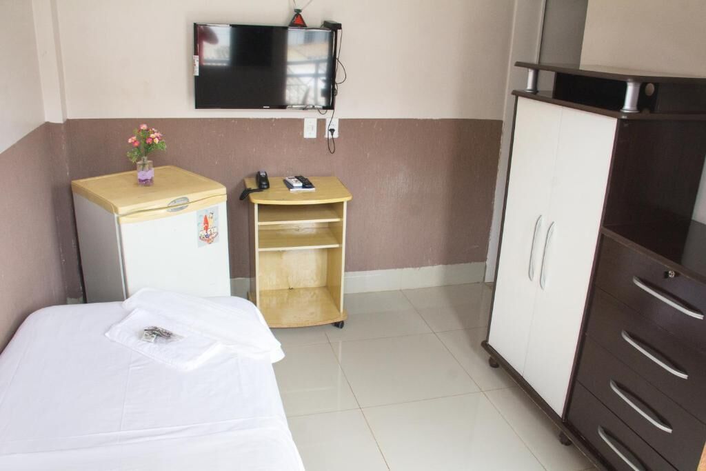 Ein Hotelzimmer mit einem Bett, einem kleinen Holzkästen, einem an der Wand befestigten Fernseher und einem Kleiderschrank.
