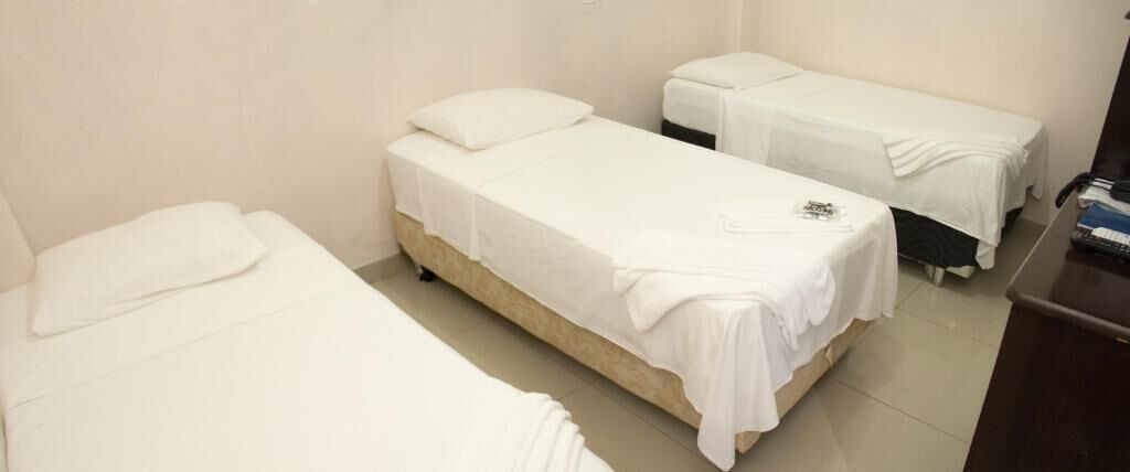 Una habitación con dos camas individuales, cada una con colchón y almohada blancos, y cabeceros de madera. Hay un escritorio con una silla y un teléfono.