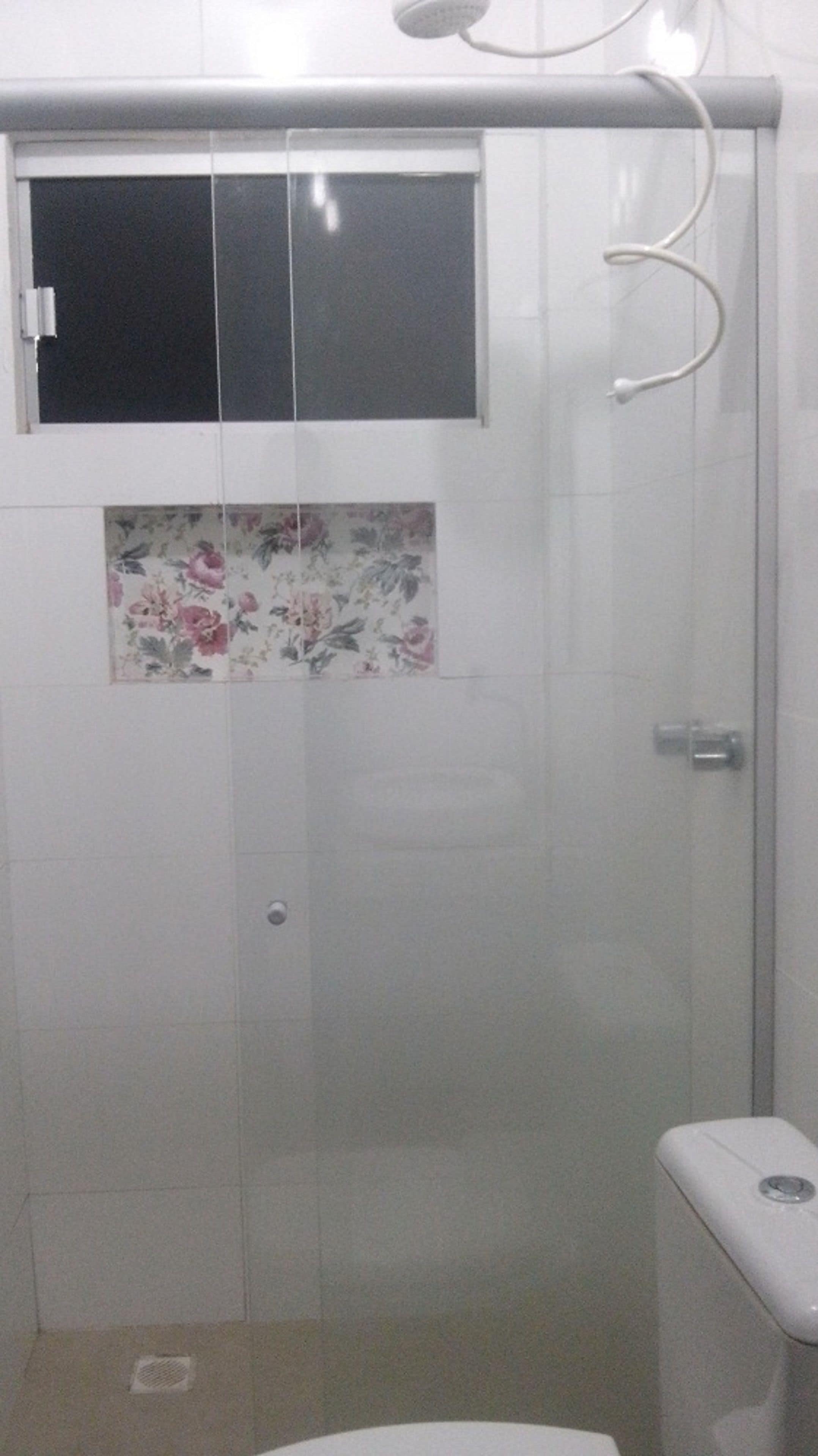 Une salle de bain avec douche, toilettes et une fenêtre ornée de motifs floraux en carreaux.